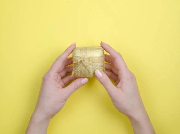 Gold-Geschenkbox mit Schleife in der Hand auf gelbem Hintergrund — Stockfoto