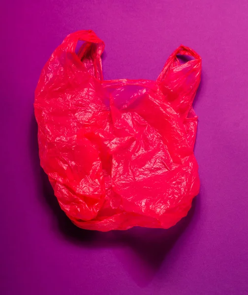 Красный пластиковый пакет на фиолетовом фоне. Яркий фон . — стоковое фото