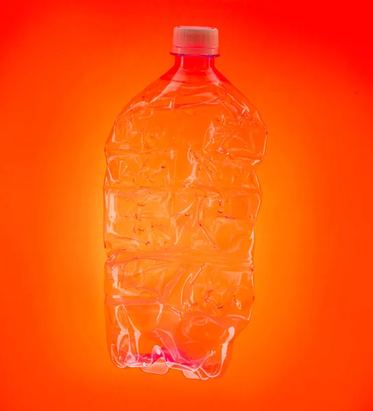 Transparent plastic crumpled bottle on orange background.