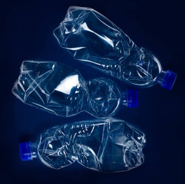 Koyu mavi bir arka plan üzerinde buruşuk plastik şişe. Plastik çöp kutusu.