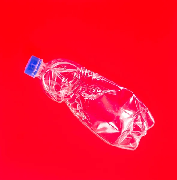 Verkruimelde doorzichtige plastic fles op een rode achtergrond. — Stockfoto