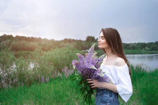 Koyu saçlı, güzel bir genç kadın. Çiçekler lupinli. Yaz arkaplanı. - Stok İmaj