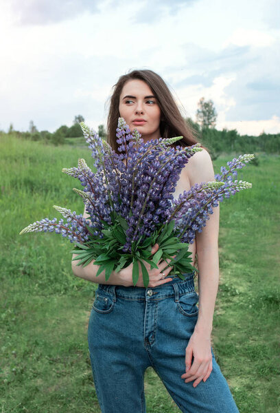 A young woman with a bouquet of lupine flowers. Beautiful woman in nature. A romantic woman.