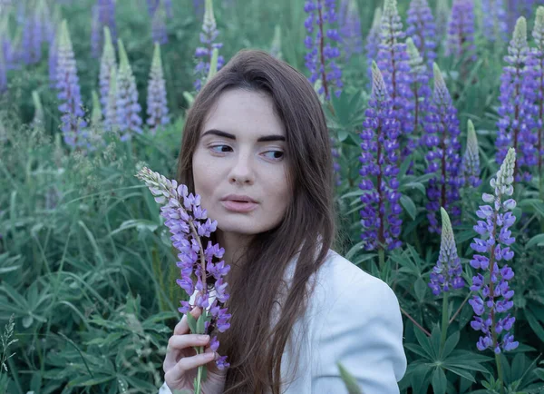 Beautiful young woman with dark hair in nature. The flowers are lupines. Summer background. — Stock Photo, Image