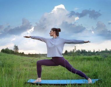 Genç bir kadın doğada yoga yapıyor. Güneşli bir akşam, güzel bir hava. Yaz zamanı..