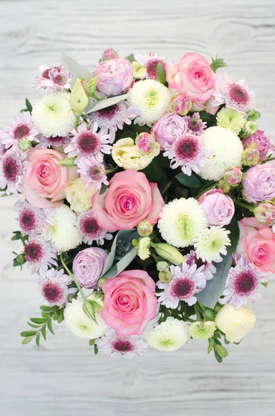The composition of flowers in the box is photographed from above. The flower arrangement consists of roses, chrysanthemum and eustoma. On the back, blurred wooden texture.