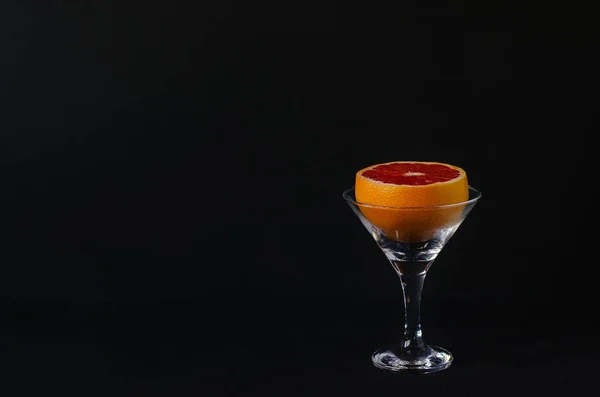 Half a grapefruit in a martini glass on a black background. It symbolizes the transition from alcohol to proper and healthy eating.