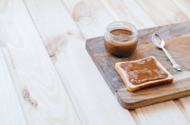 Tost ve kavanoz fıstık ezmesi bir ahşap tahta üzerinde. Yakınlarda bir çay kaşığı retro tarzı olduğunu.