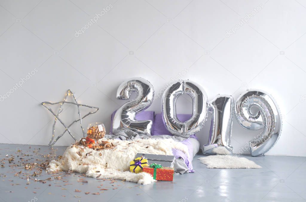 The big numbers of balloons with the new year 2019. The composition consists of a bed, pillows, a tray with tangerines and croissants and a festive star with a garland.