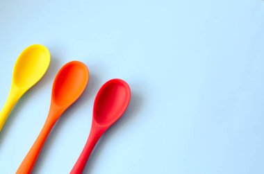 Düz renkli parlak mutfak kaşıkları mavi bir arka plan üzerinde.