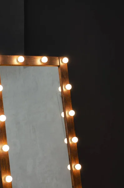 Large mirror with light bulbs against a black wall.