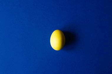 Mavi bir arka plan üzerinde sarı renkli bir Paskalya yumurtası. Minimalizm.