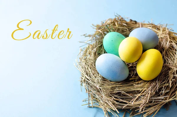 Multi-colored Easter eggs in a nest on a blue background. With the text Easter.