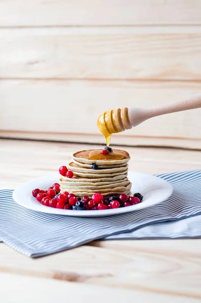 Een stapel pannenkoeken met bessen en honing op een witte plaat. — Stockfoto