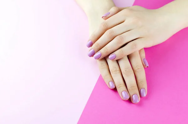 Kobiece ręce z fioletowym manicure na różowym tle. — Zdjęcie stockowe