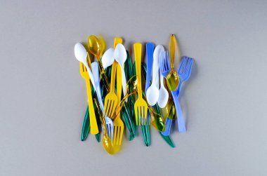 Gri bir arka plan üzerinde plastik çatal, kaşık ve bıçaklar.