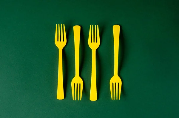 Plastic yellow forks on a green background. — Stock Photo, Image