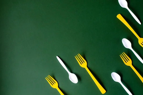 Plastic yellow forks and white spoons on a green background. — Stock Photo, Image