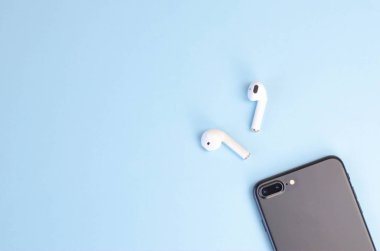 Mavi arka planda akıllı telefonu olan kablosuz beyaz kulaklıklar.. 