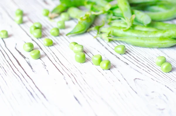 Young peas in pods and without on a light wooden background.