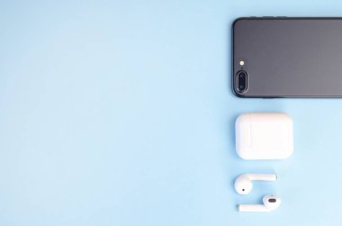 Mavi arka planda akıllı telefonu olan kablosuz beyaz kulaklıklar.. 