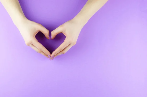 Female hands with a purple manicure in the form of a heart.