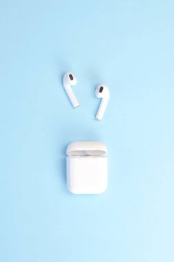 Wireless white headphones with a case on a blue background. clipart