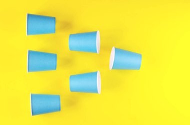 Parlak sarı arka planda mavi kağıt bardaklar.