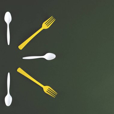 Yeşil bir arka plan üzerinde plastik sarı çatal ve beyaz kaşık. 