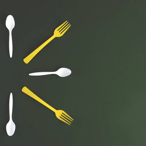 Plastic yellow forks and white spoons on a green background. — Stock Photo, Image