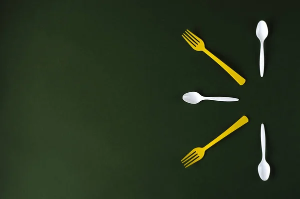 Plastic yellow forks and white spoons on a green background. — Stock Photo, Image