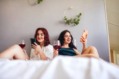 Pijamalı kızlar ellerinde telefon ve şarapla yatakta oturuyorlar. Pijama partisi. Kızlar partisi..