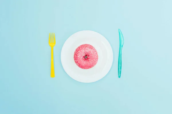 Bright pink donut on a blue plate and light blue background. Sweet and delicious food.