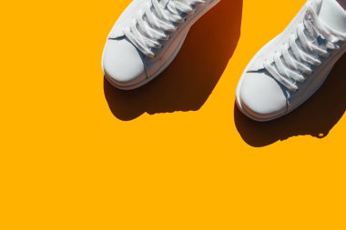 Turuncu arka planda sert gölgeli beyaz spor ayakkabılar. Şık spor ayakkabıları..