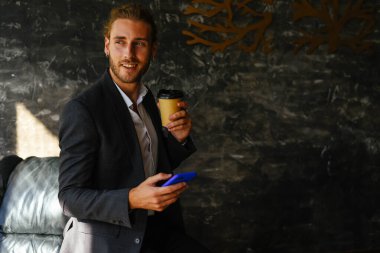 Elinde telefon ve kahve olan takım elbiseli bir adam.. 