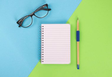 Spiral Not defteri, kalem ve pastel arka plan üzerinde gözlük.