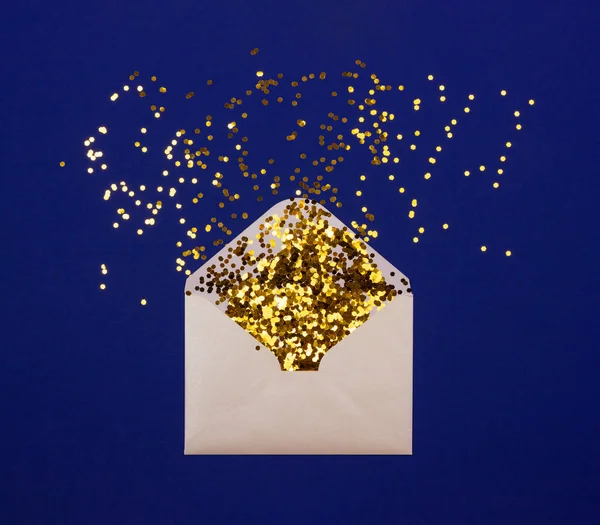 Gouden confetti verspreid van de envelop op blauwe achtergrond. — Stockfoto