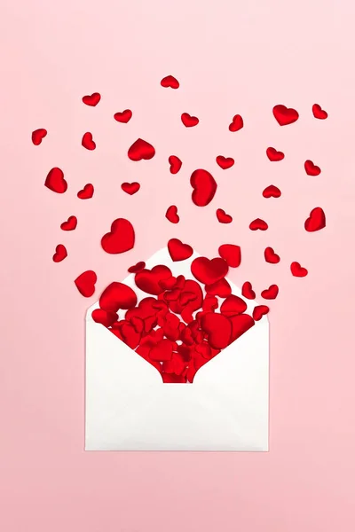 Festive background for Valentines day with red hearts scattered from envelope on pink background.