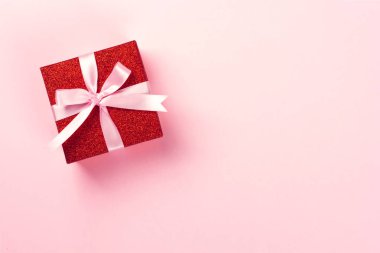 Pembe arka planda pembe kurdeleli kırmızı hediye kutusu.