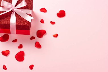 Pembe arka planda pembe kurdeleli kırmızı hediye kutusu.