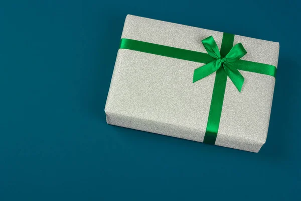 Doos van de gift van de grijze glitter met groene lint op blauwe achtergrond. — Stockfoto