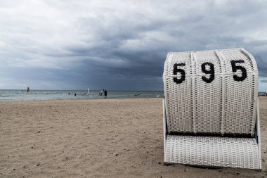 Bulutlu bir günde, Almanya 'nın Baltık Denizi' ndeki kumlu sahilde beyaz bir hasır plaj sandalyesinin görüntüsü. Malzemesiz Kraliyet fotoğrafı..