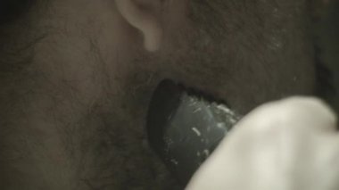 Adam banyo aynasının önünde tıraş makinesiyle sakalını tıraş ediyor. Yakın plan.