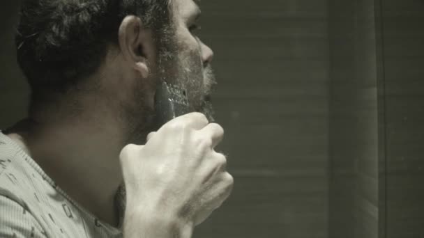 Gość goli brodę przycinaczem przed lustrem w łazience. — Wideo stockowe