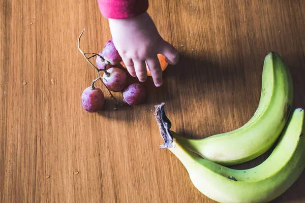 Mano del bebé manipulando diferentes frutas en una mesa de madera — Foto de Stock