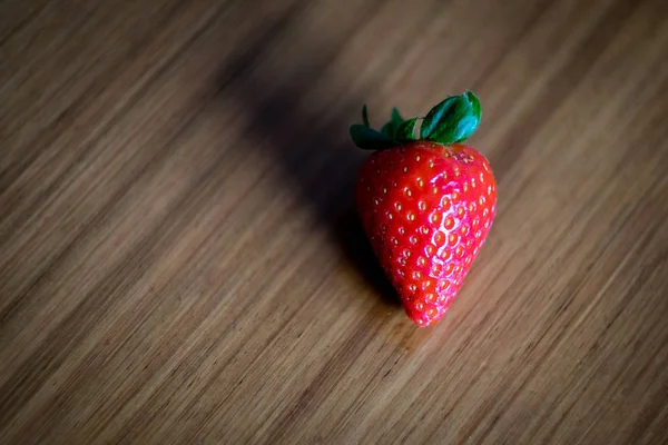 Intensiv rote Erdbeere steht auf einem holzgesäumten Tisch — Stockfoto