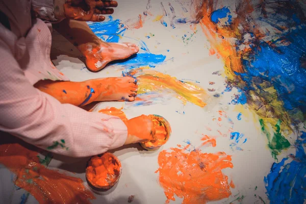Manos y pies de niño cubiertos de pinturas coloridas en una alfombra de papel — Foto de Stock