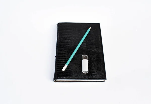 Black notebook with a green pencil and a flash drive on a white background