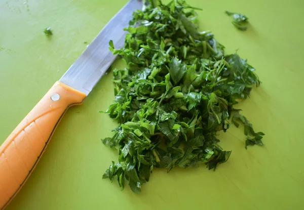 A green board with finely chopped greens and a yellow knife.