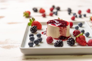 Berry soslu lezzetli İtalyan tatlı panna cotta, beyaz ahşap backgroun taze çilek